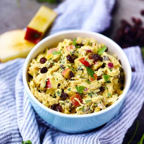 A bowl of curried chicken salad with apples and raisins in the background on a towel.