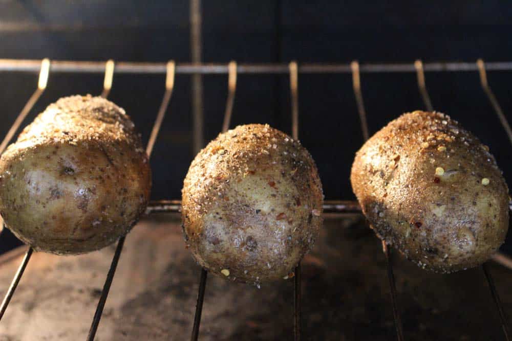 Inside of an oven, with three potatoes placed directly on the wire oven rack.