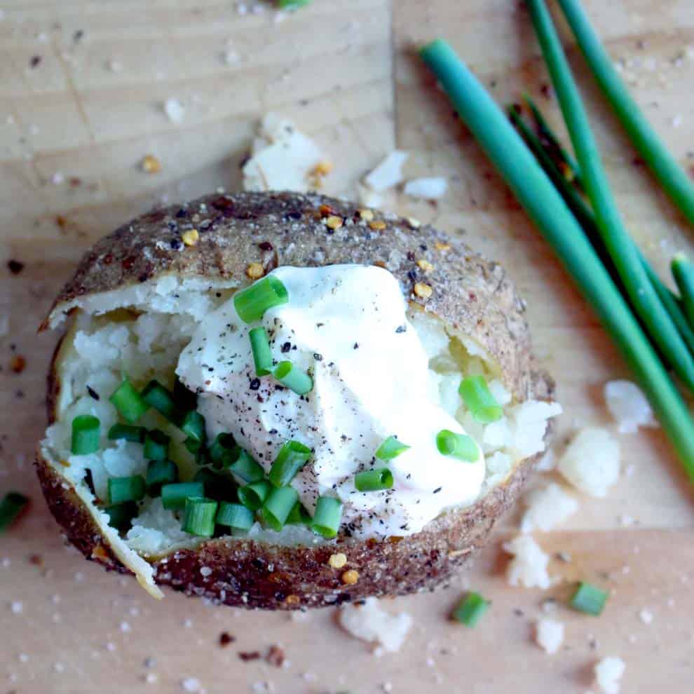 Bird's eye view of a potato that has been sliced open and topped with sour cream, salt and pepper, and chopped green onions.