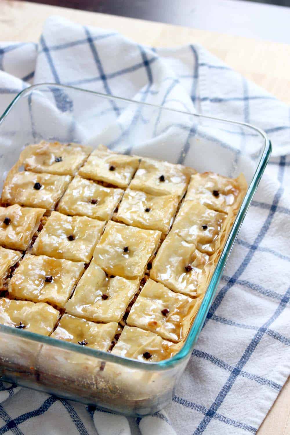 A glass casserole dish holding baklava that has been cut into squares and garnished with cloves.