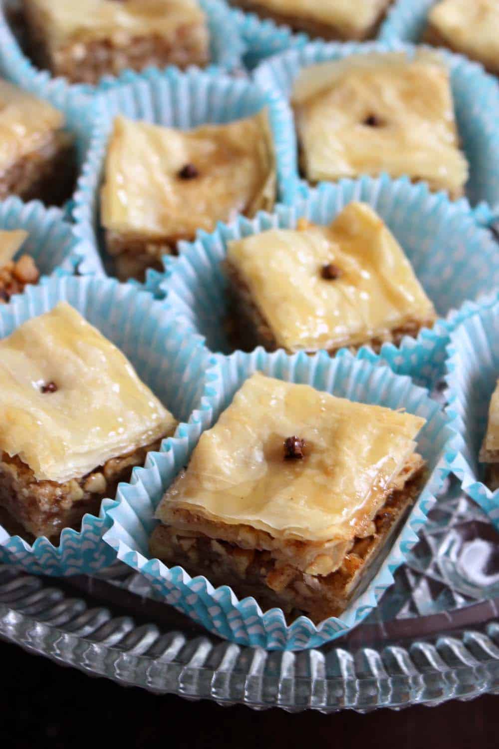 Close up of baklava squares in cupcake liners, and each garnished with a clove.