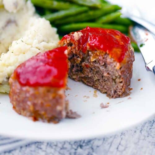 Square photo of a mini meatloaf sliced in half with green beans and potatoes.