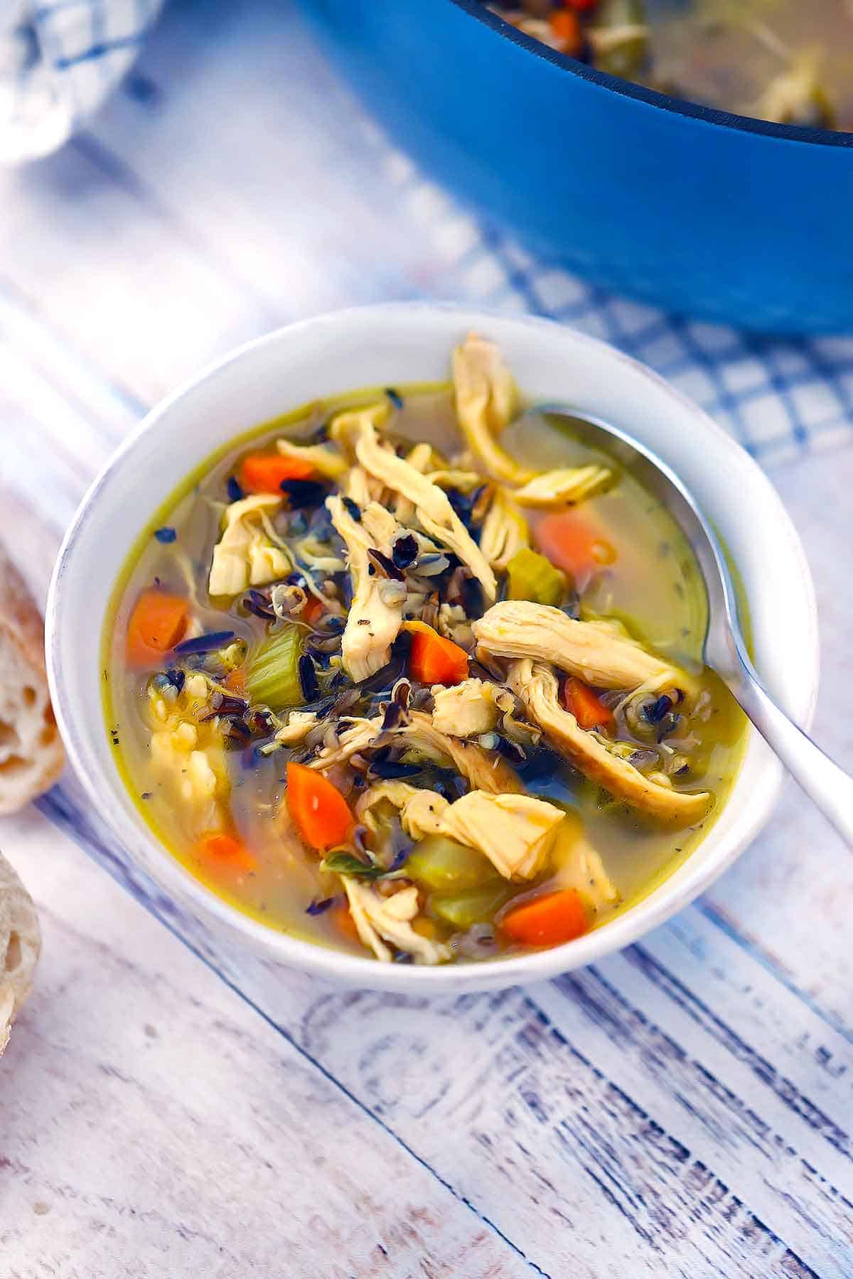 A white bowl of chicken wild rice soup with a spoon in it.