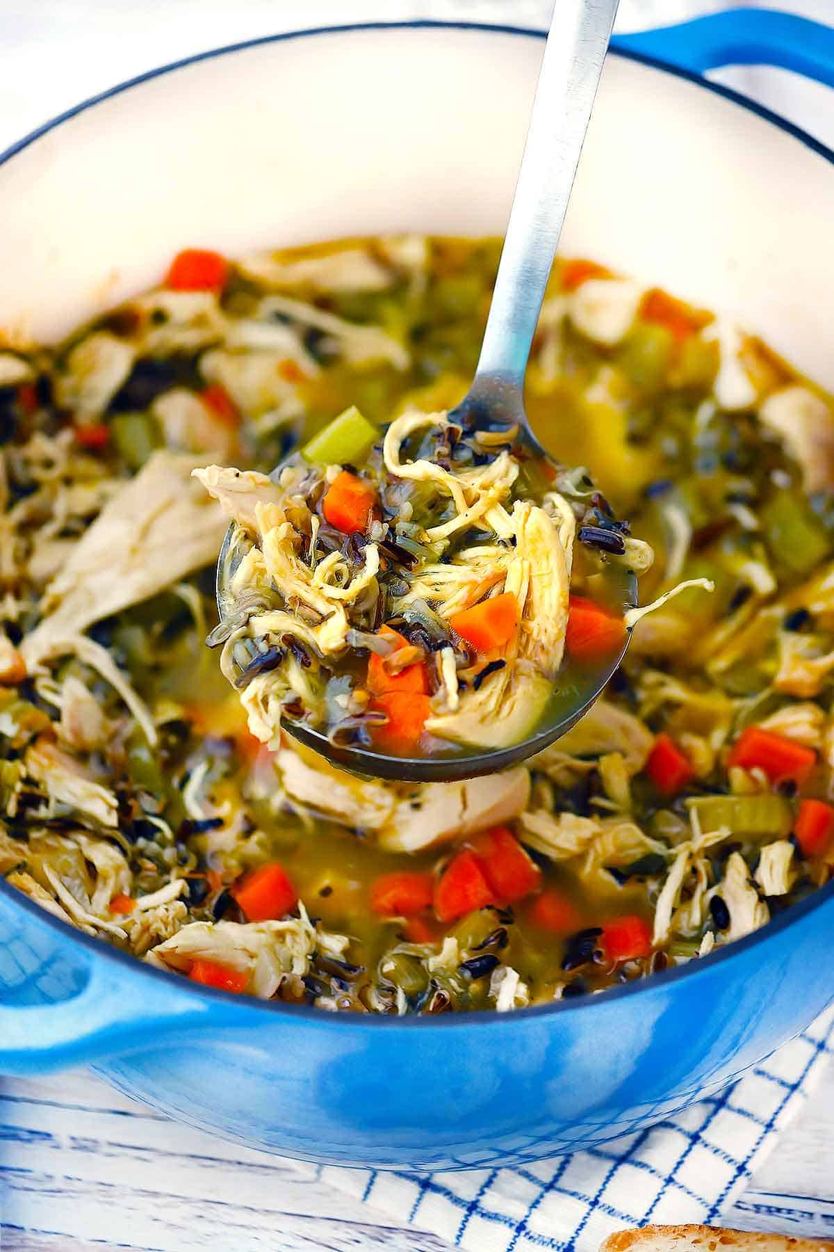 A blue Dutch oven with a ladle scooping out chicken wild rice soup.