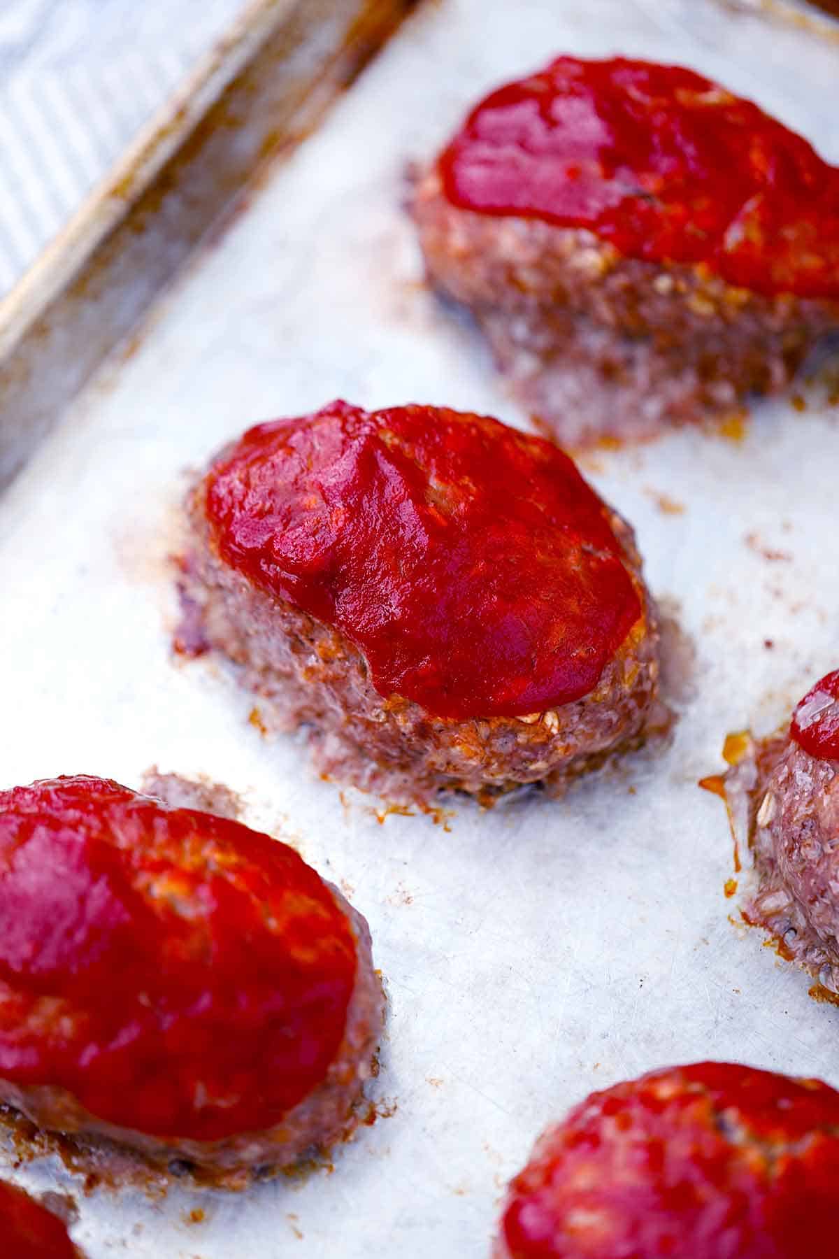 Mini meatloaves topped with ketchup on a baking sheet.
