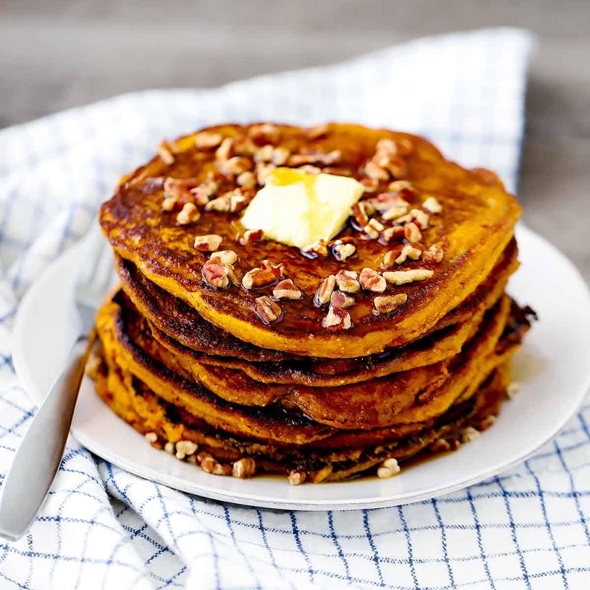A plate with pumpkin pancakes sprinkled with pecans and a tab of butter.