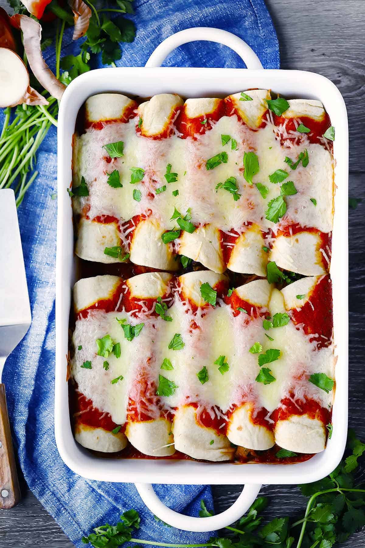 A white baking dish on a blue towel with enchiladas inside.