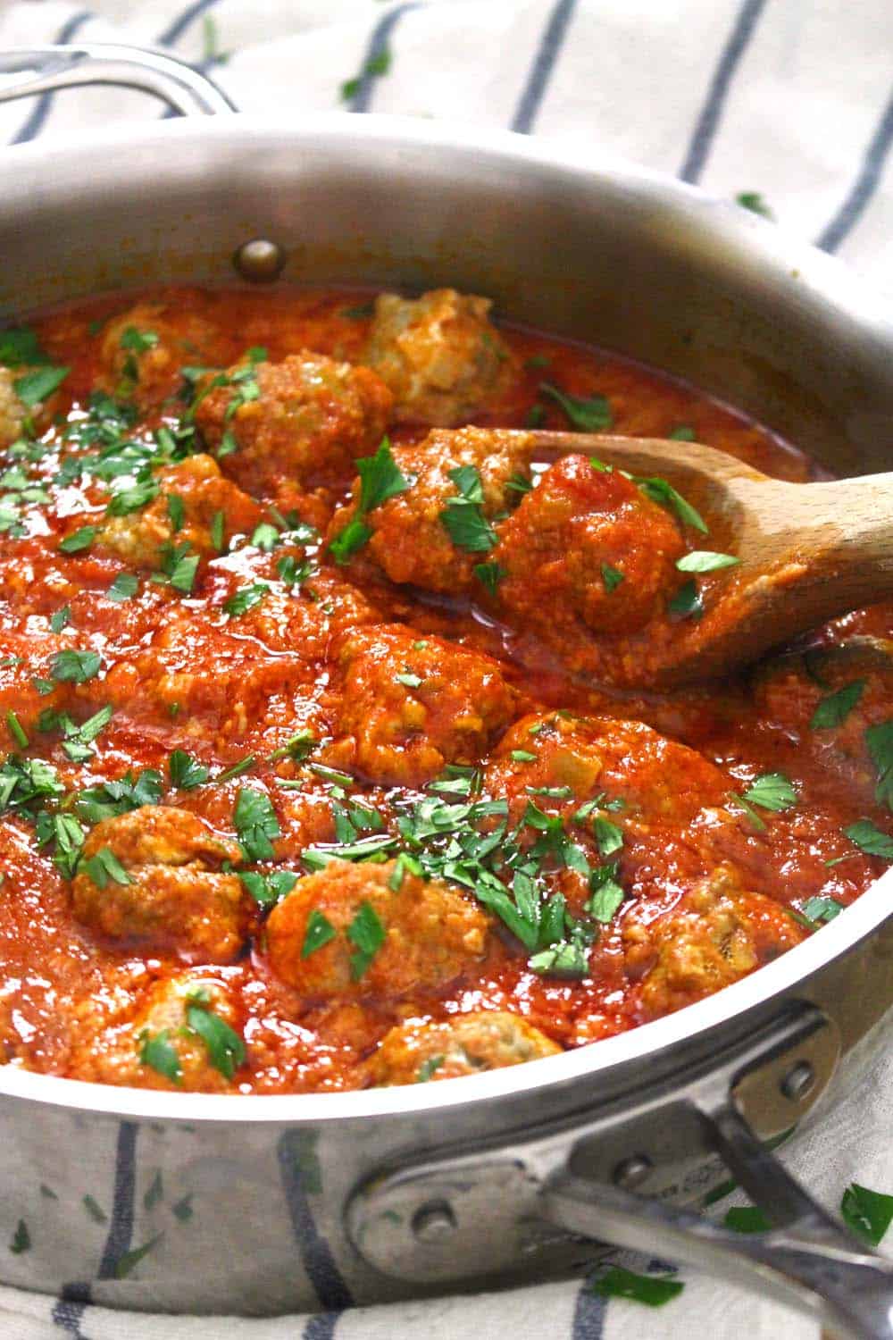 Tomato sauce and meatballs in a metal skillet, with a wooden spoon perched on the edge.