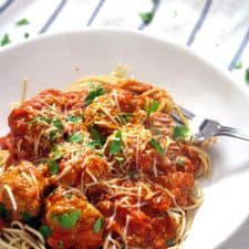 White plate holding spaghetti and meatballs, with a metal work perched on the edge of the plate.