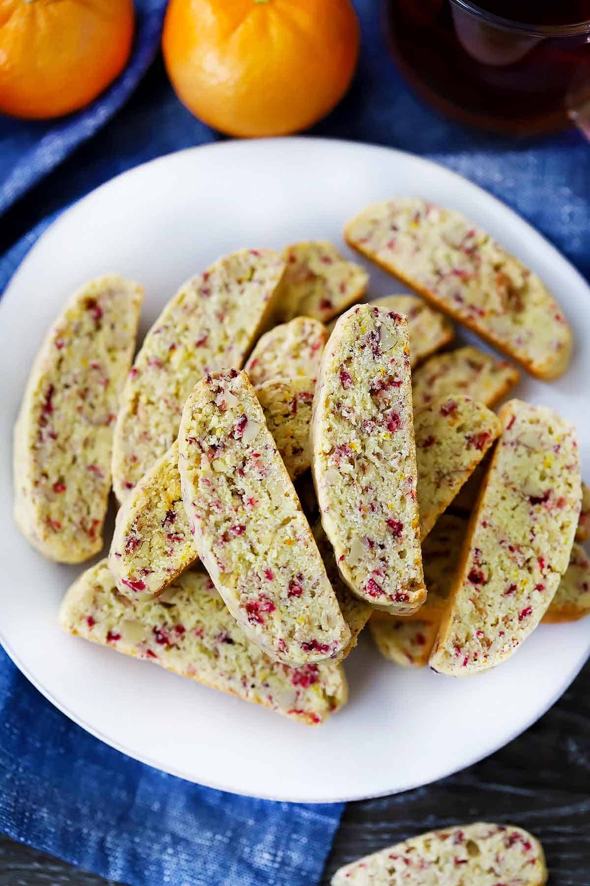 An overhead photo of cranberry orange biscotti on a white plate with a blue towel.