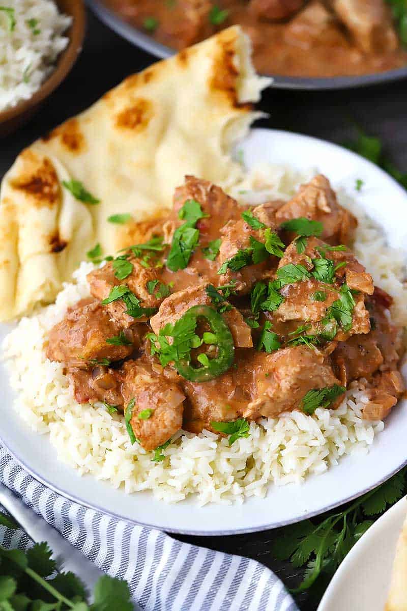 A white plate with rice, chicken tikka masala, and naan.