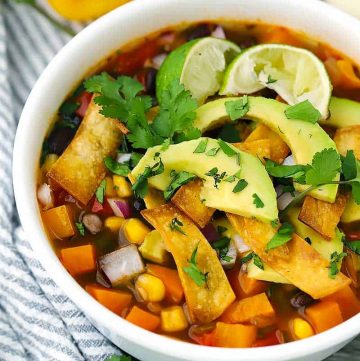 Close up photo of a bowl of vegetarian tortilla soup with avocado, sweet potato, cilantro, and lime.