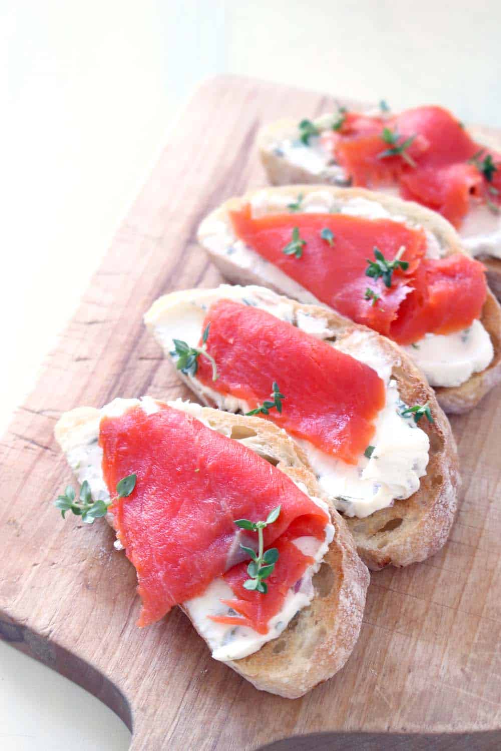 A row of four cream cheese and salmon toasts on a wooden cutting board.