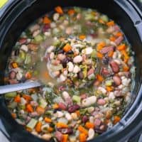 A ladle in a slow cooker with 15 bean soup.