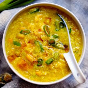 Square overhead photo of egg drop soup with corn in a white bowl with soup spoon.