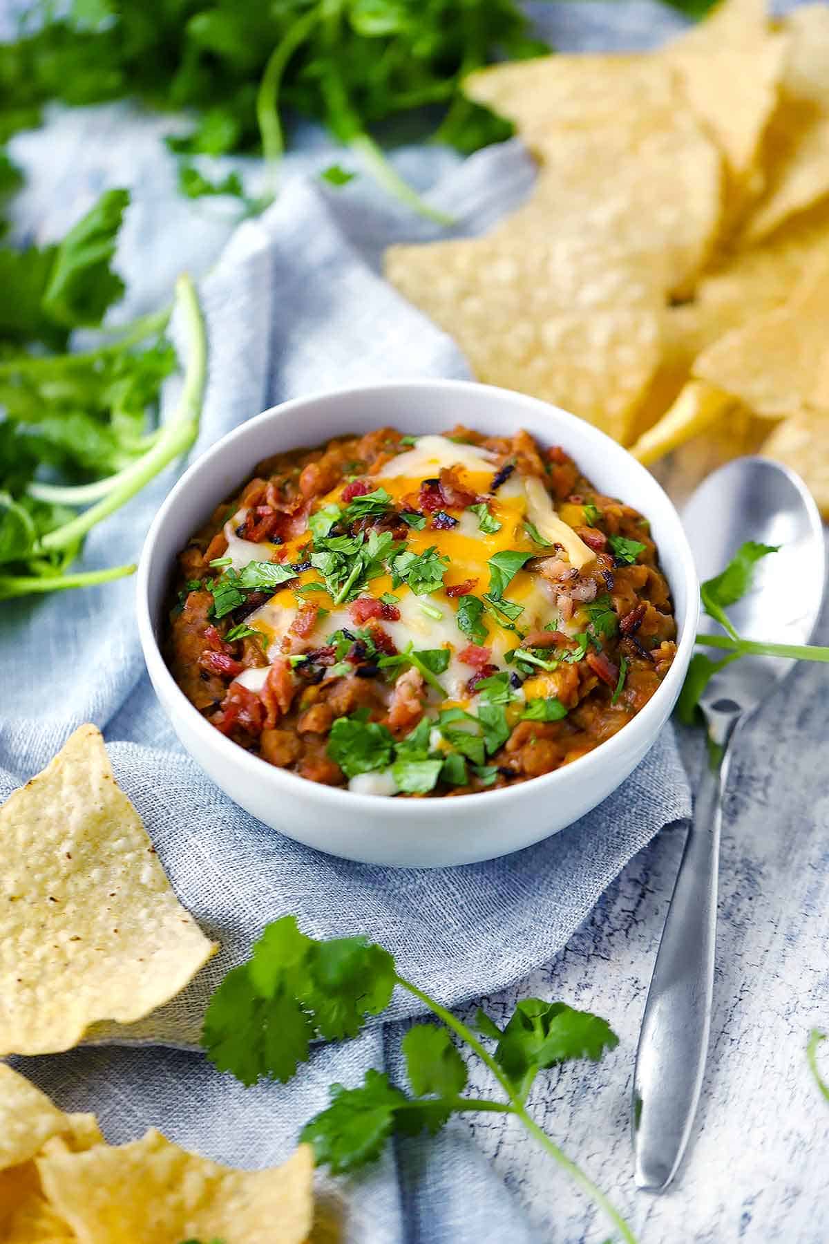 A white bowl with refried beans and tortilla chips and cilantro scattered around.