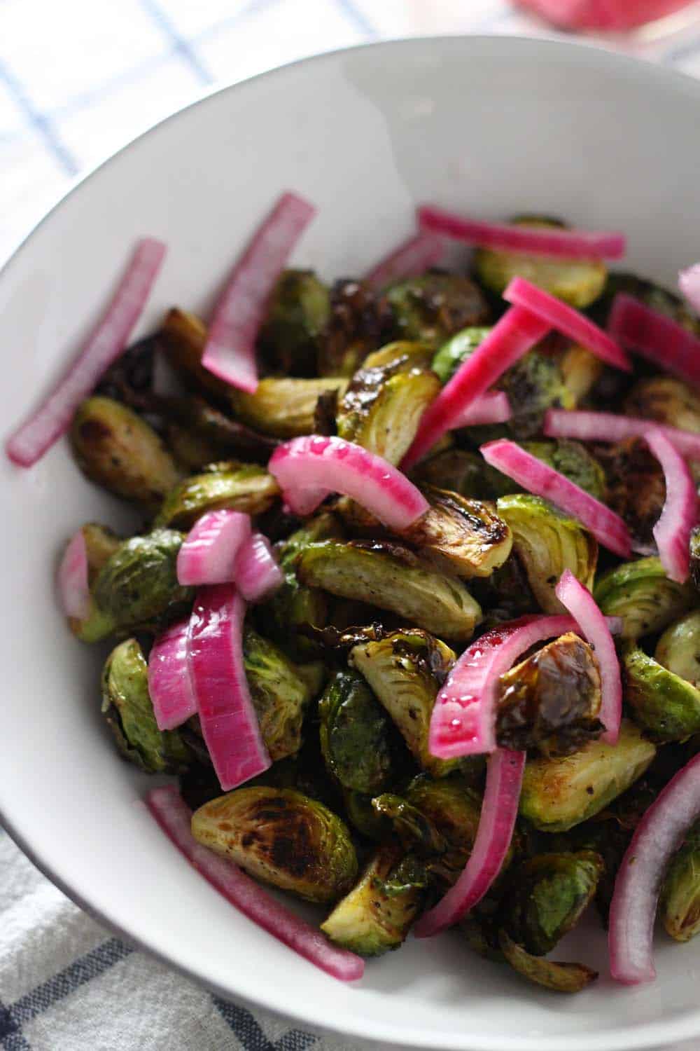 Close up bird's eye view of a white bowl holding crispy brussels sprouts with picked red onion.