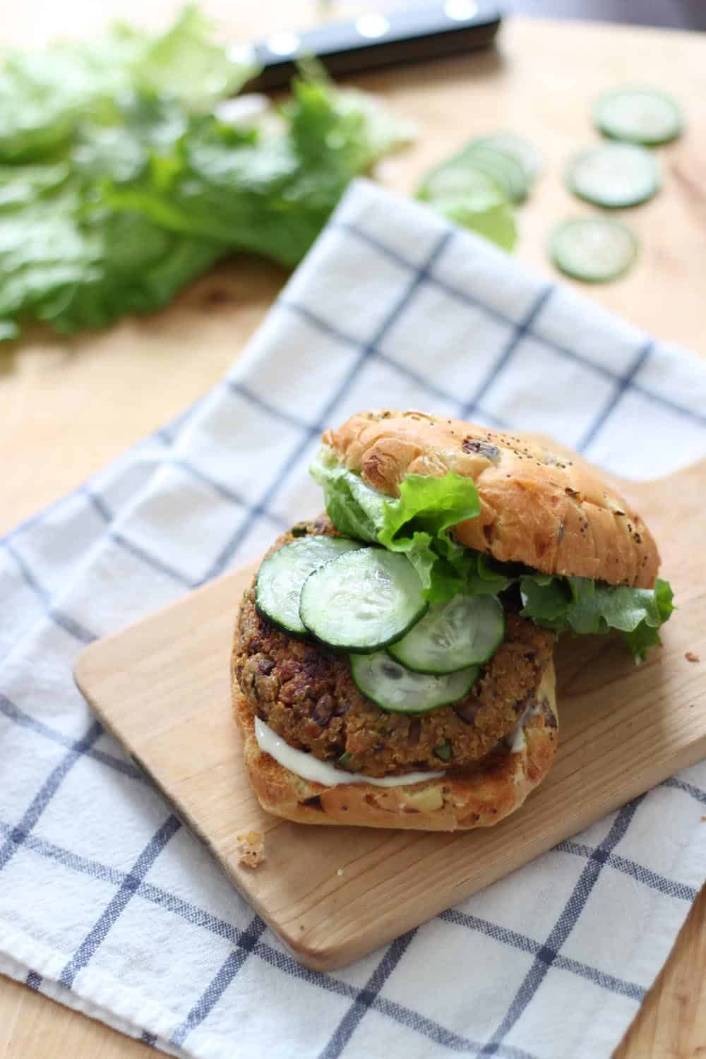 Veggie burger with the top bun pushed aside to show toppings, on a wooden cutting board, on a blue and white checkered cloth.