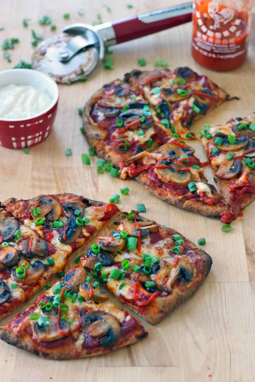 Two Buffalo mushroom naan pizzas on a wooden cutting board, each cut into fourths, with chopped scallions and ingredients scattered around.