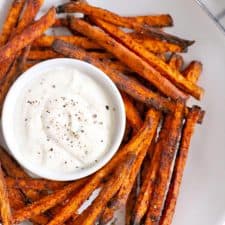 Bird's eye view of chili fries on a white plate, with a ramekin of creamy white dipping sauce.