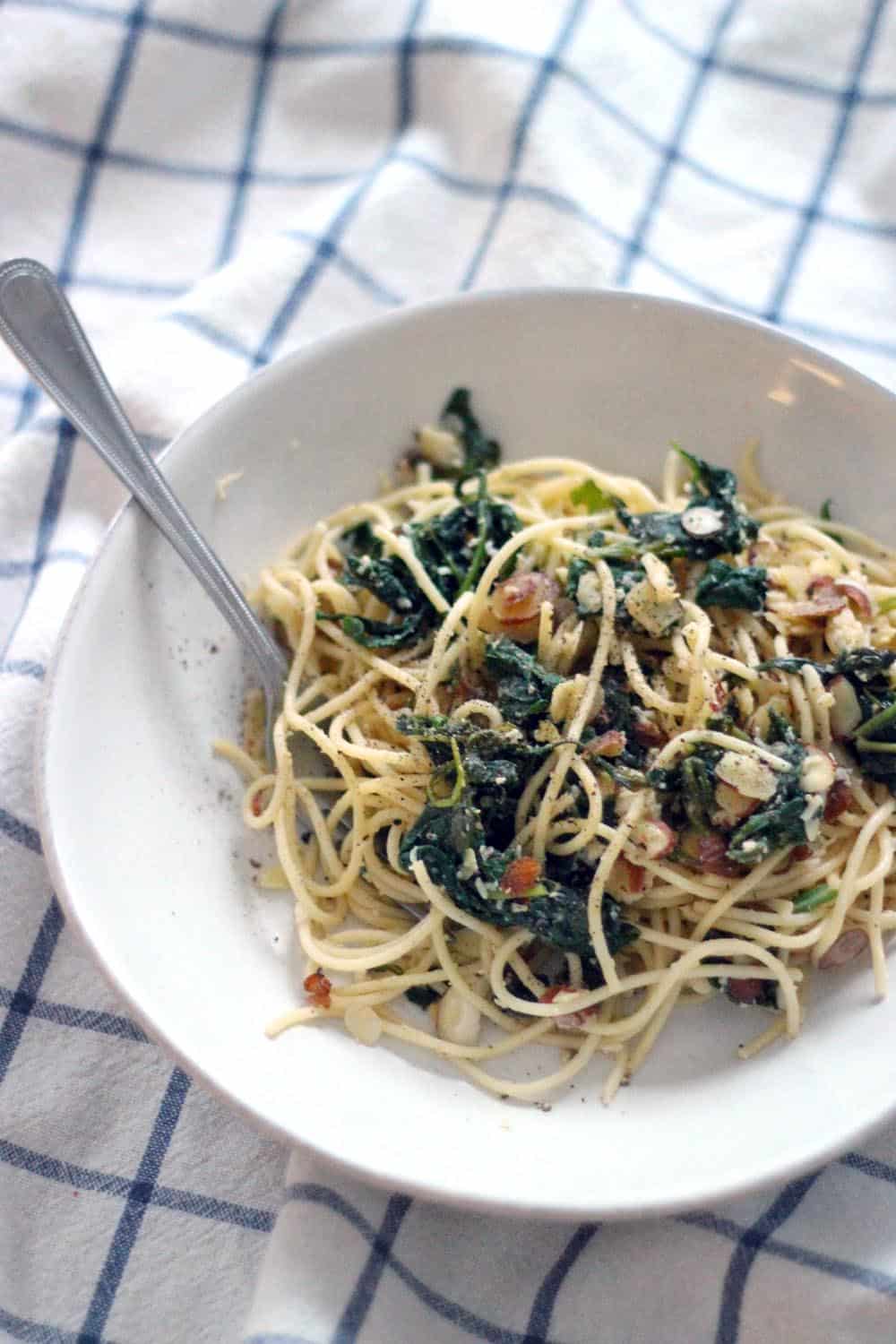 Bird's eye view of spaghetti with wilted greens and browned butter sauce in a white bowl.