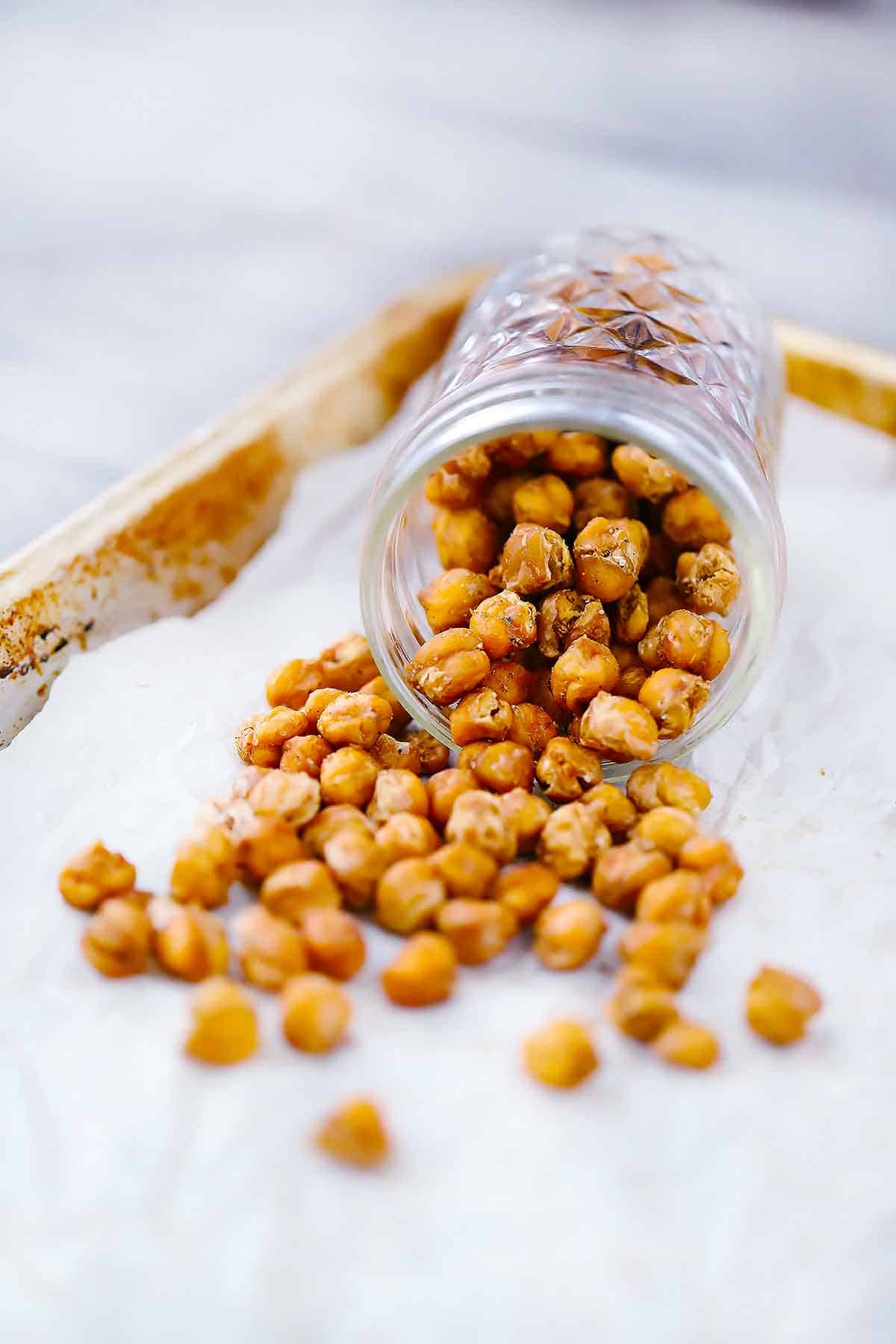 Roasted chickpeas coming out of a mason jar onto a parchment covered baking sheet.