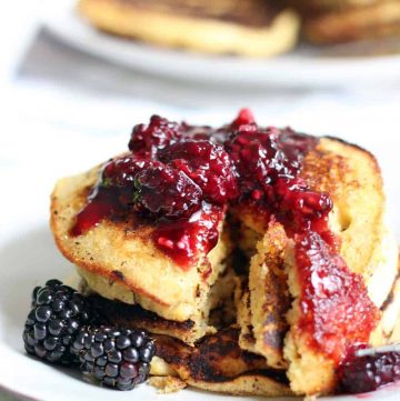 Stack of pancakes topped with blackberry maple syrup, with a triangular slice cut through all pancakes.