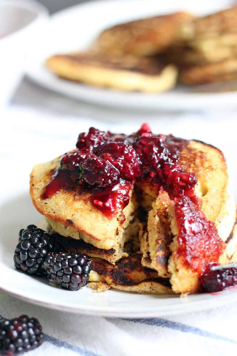 Stack of pancakes topped with blackberry maple syrup, with a triangular slice cut through all pancakes.