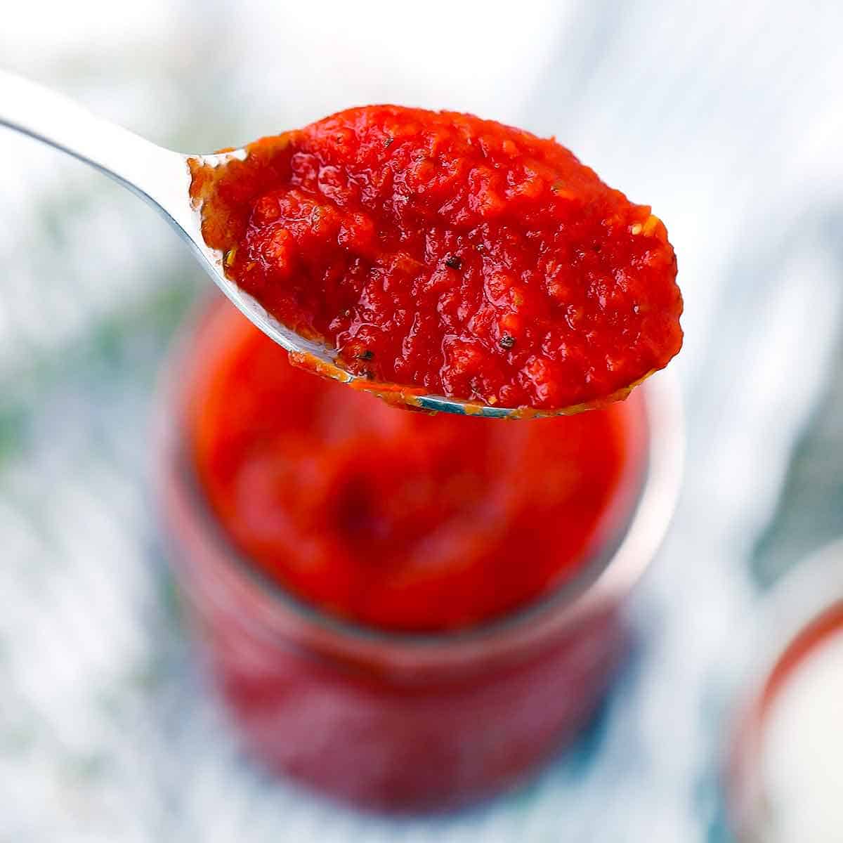 A spoonful of pizza sauce over a mason jar.