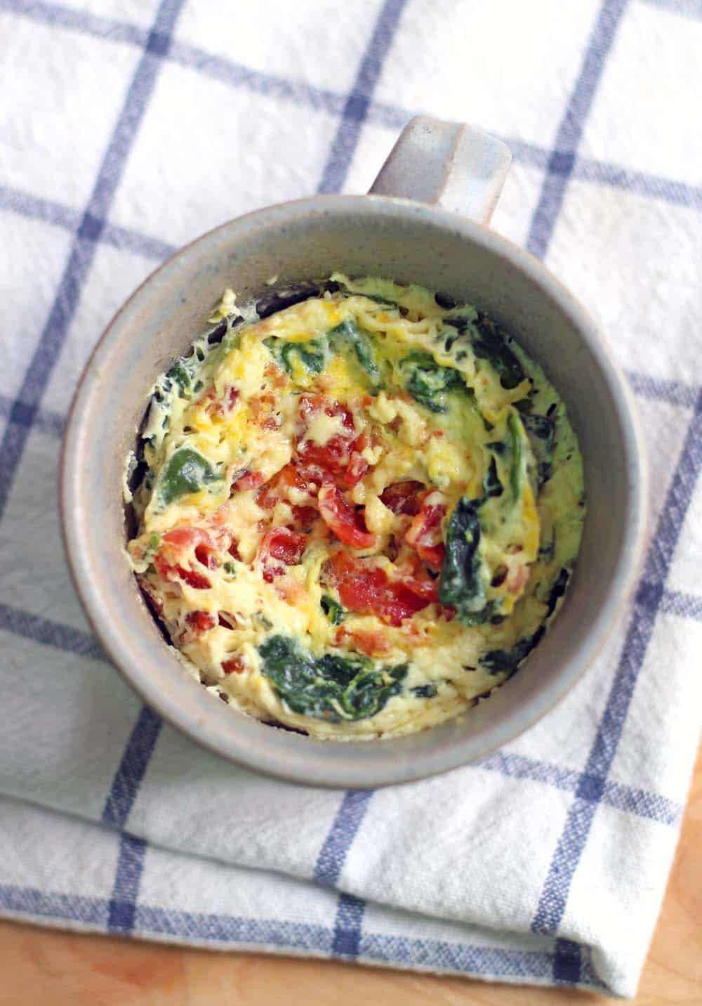 Bird's eye view of spinach and cheddar microwave quiche in a mug, which rests on a blue and white checkered cloth.