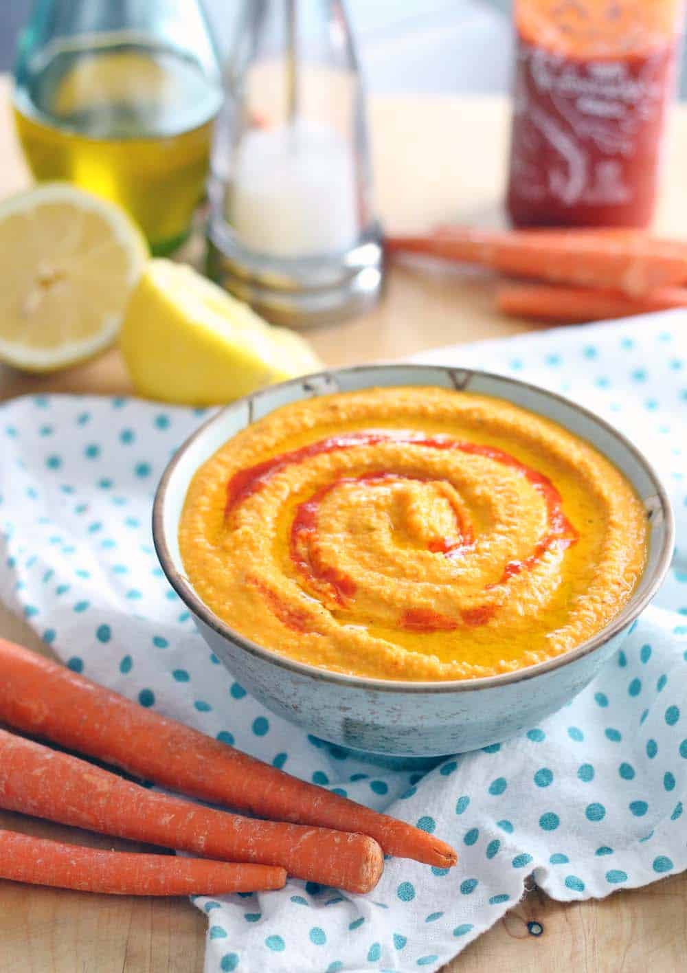 Sriracha Carrot Hummus in a bowl, with ingredients scattered around.