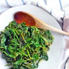 sautéed spinach with lemon and garlic on a white plate with a wooden spoon.