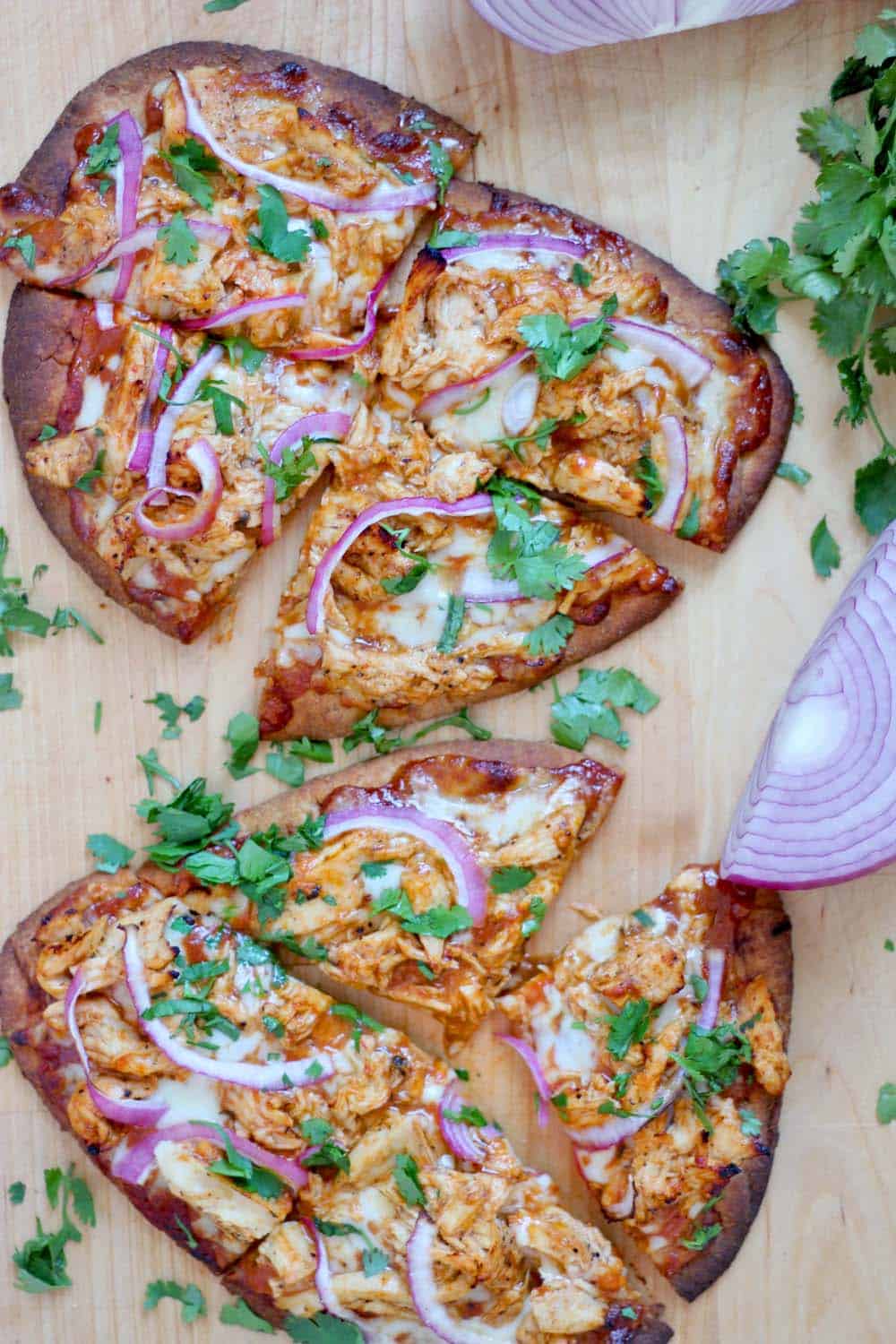 Bird's eye view of two BBQ Chicken Naan Pizzas on a wooden cutting board.