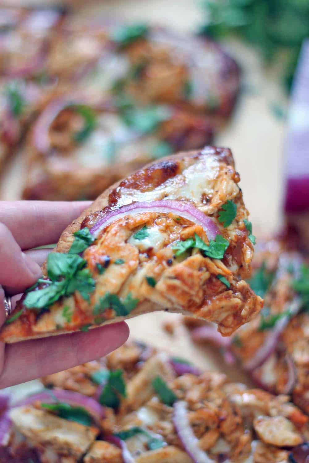 Close of up of a hand holding a slice of BBQ Chicken Naan Pizza.