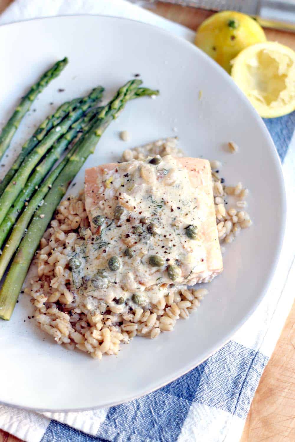 Bird's eye view of white plate holding Garlic Poached Salmon with Creamy Lemon Caper Sauce over rice, with asparagus on the side.
