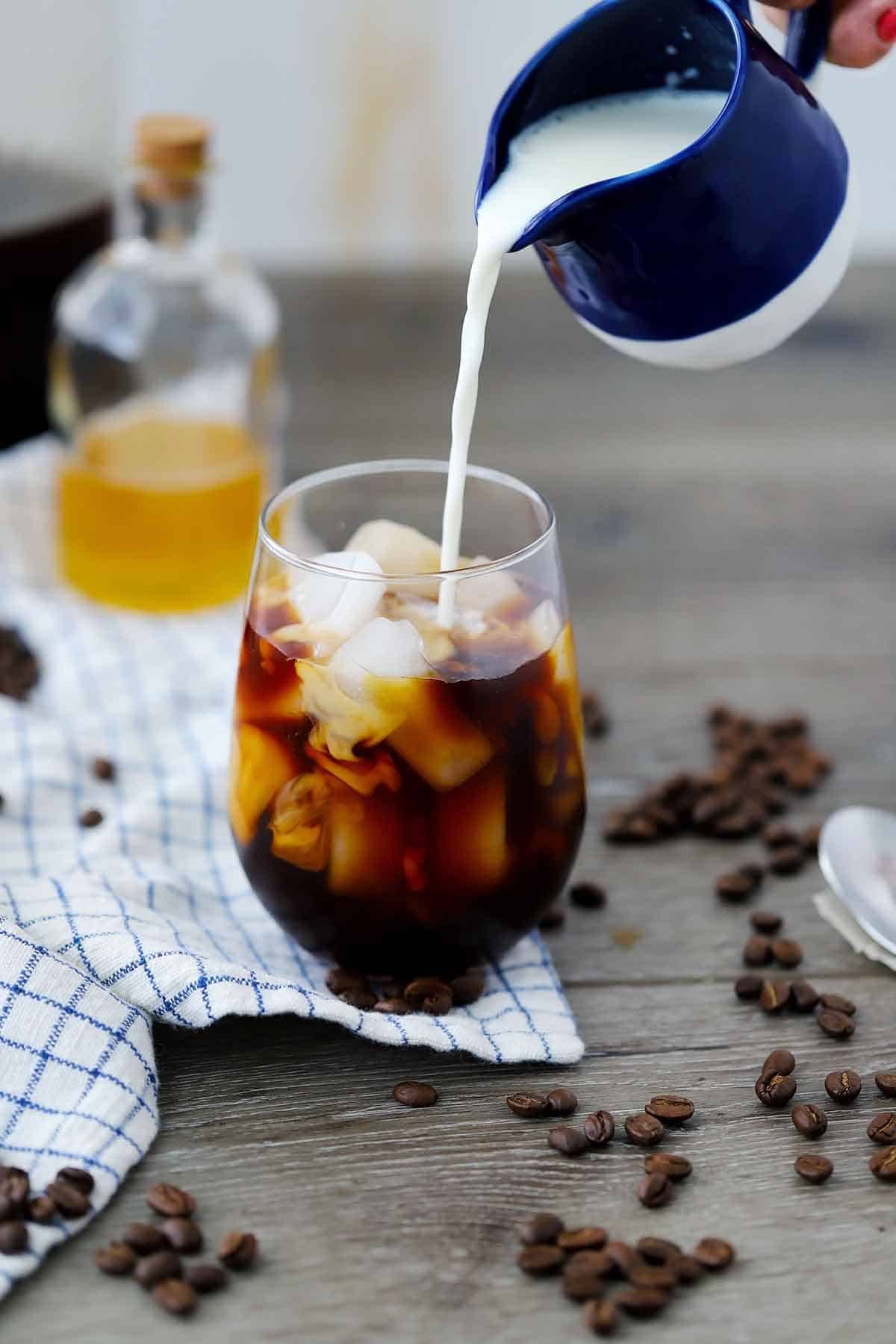 Pouring whole milk into an iced coffee.