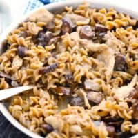 A skillet with healthy chicken and mushroom stroganoff and a spoon scooping some out.