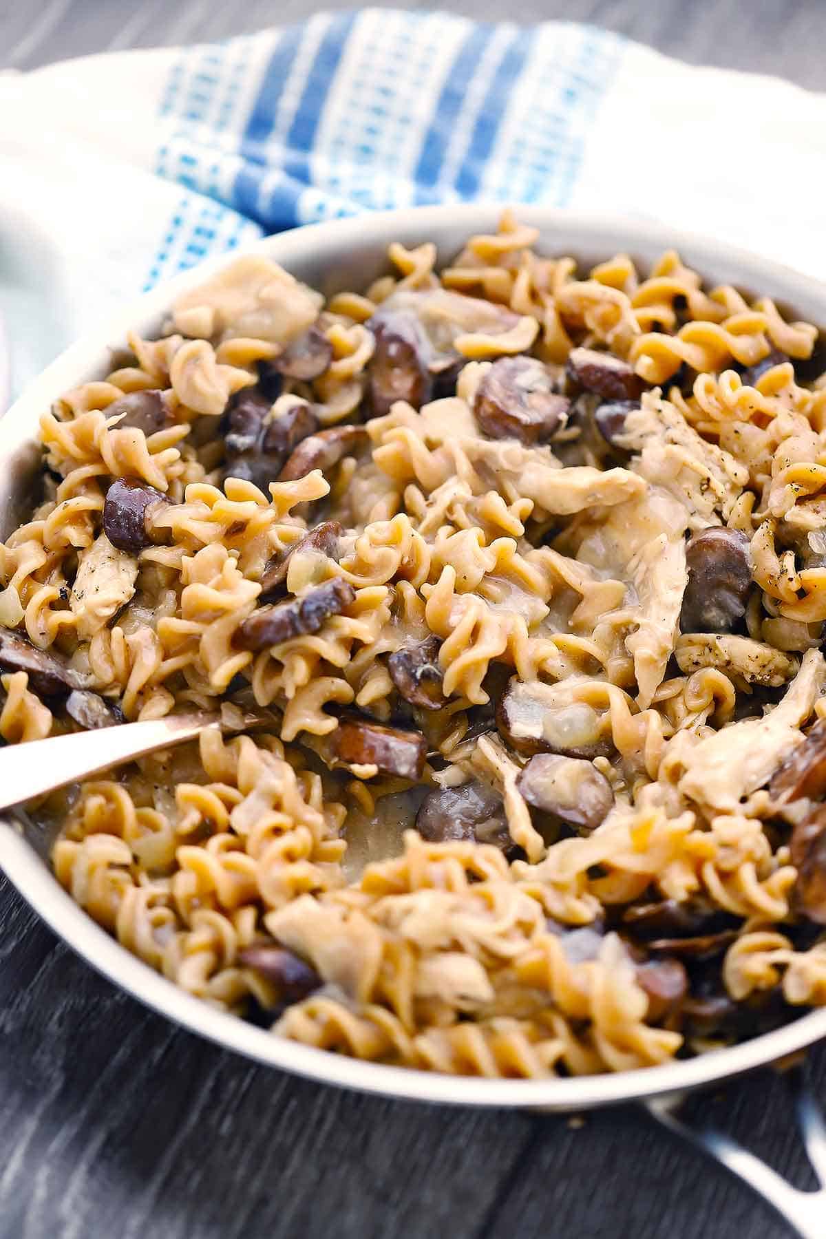 A skillet with healthy chicken and mushroom stroganoff and a spoon scooping some out.