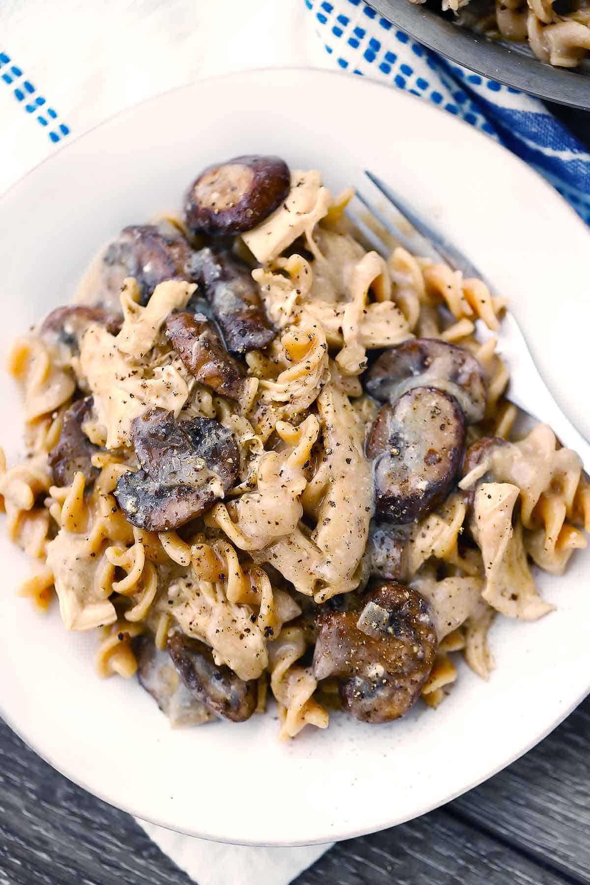 Chicken and mushroom stroganoff on a white plate with a fork and black pepper on top.