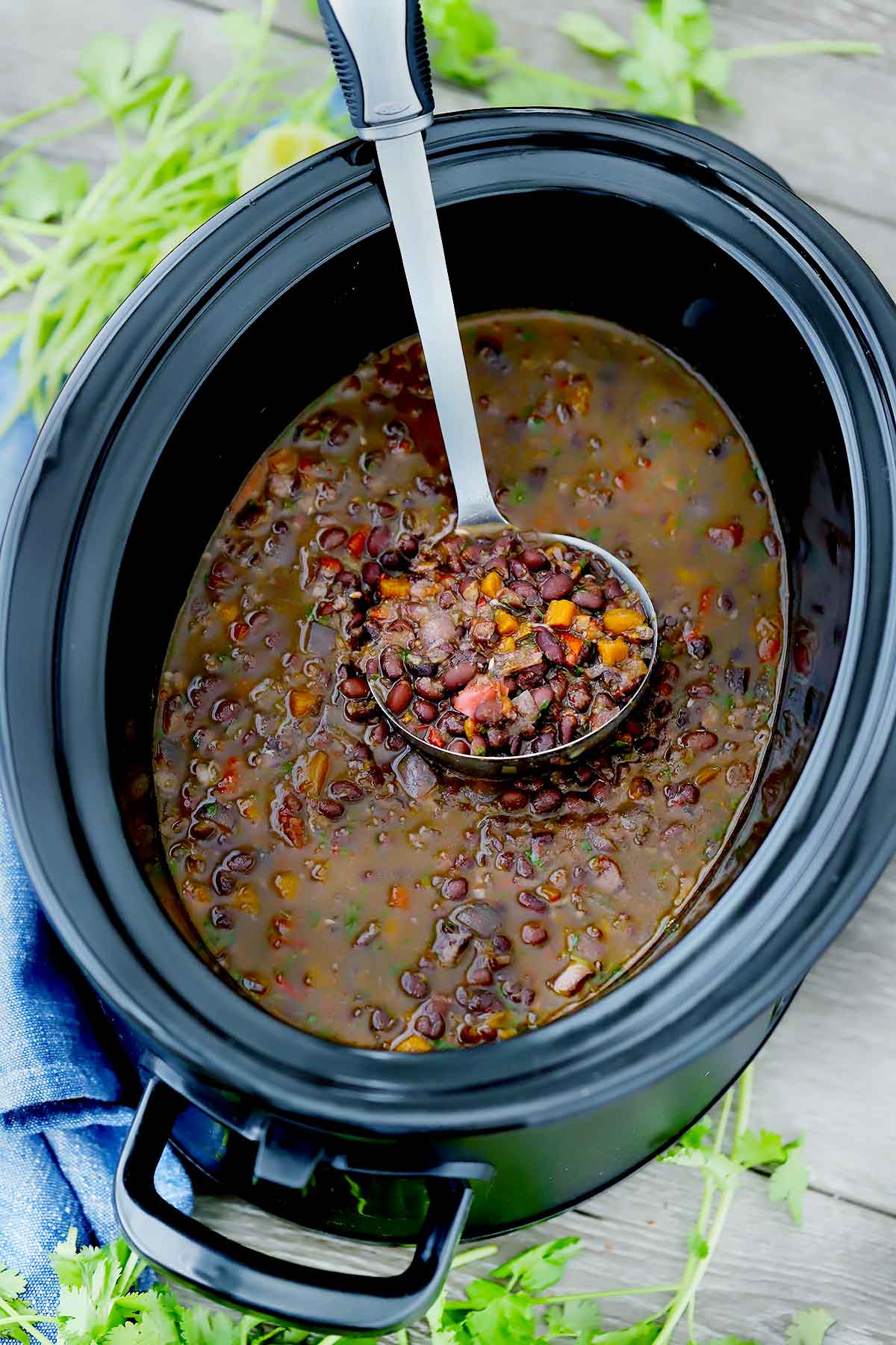 A slow cooker with black bean soup and a ladle.