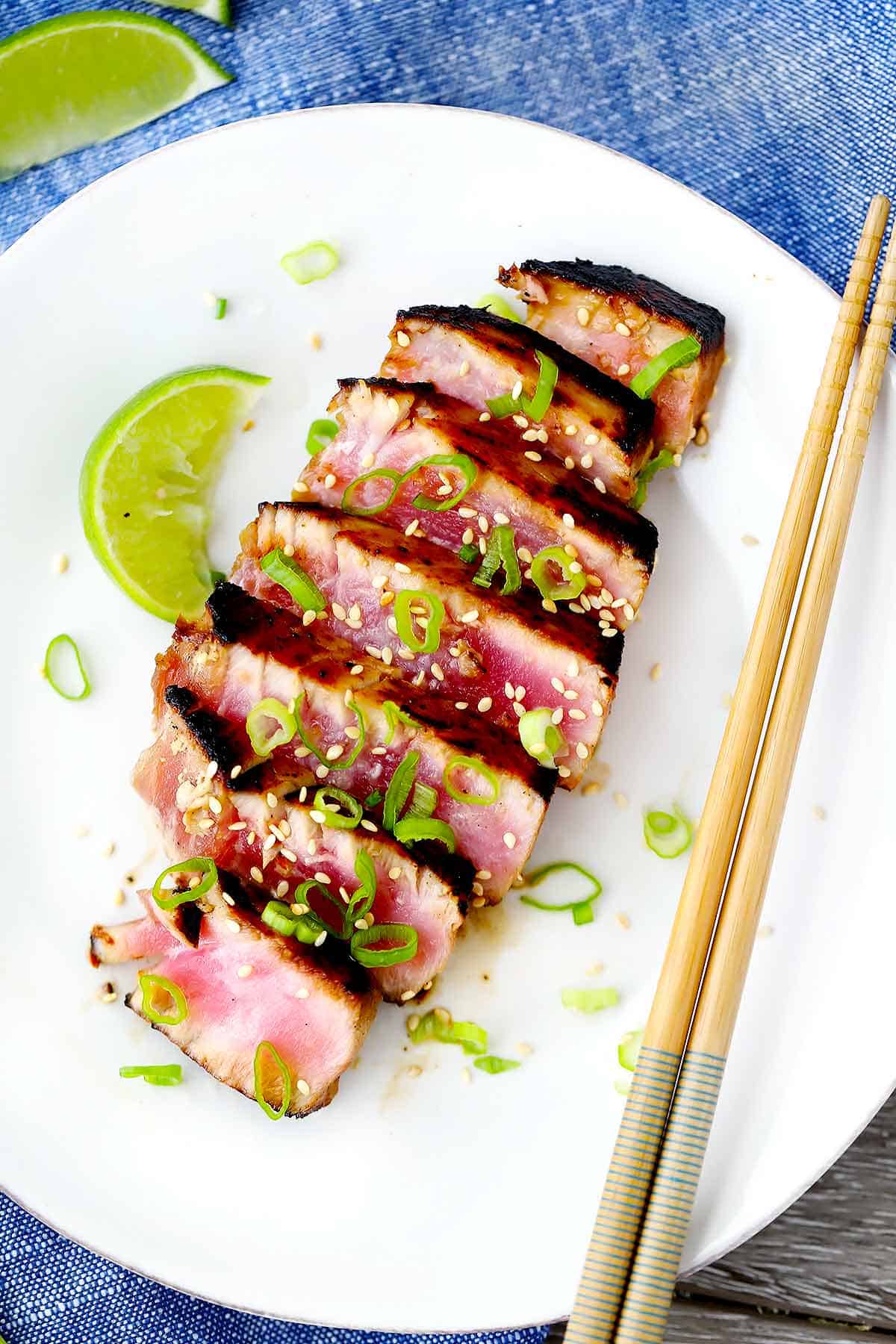 A plate with seared ahi tuna steak, chopsticks, a lime wedge, and scallions.