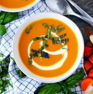 An overhead photo of a bowl of carrot ginger soup garnished with fresh basil.