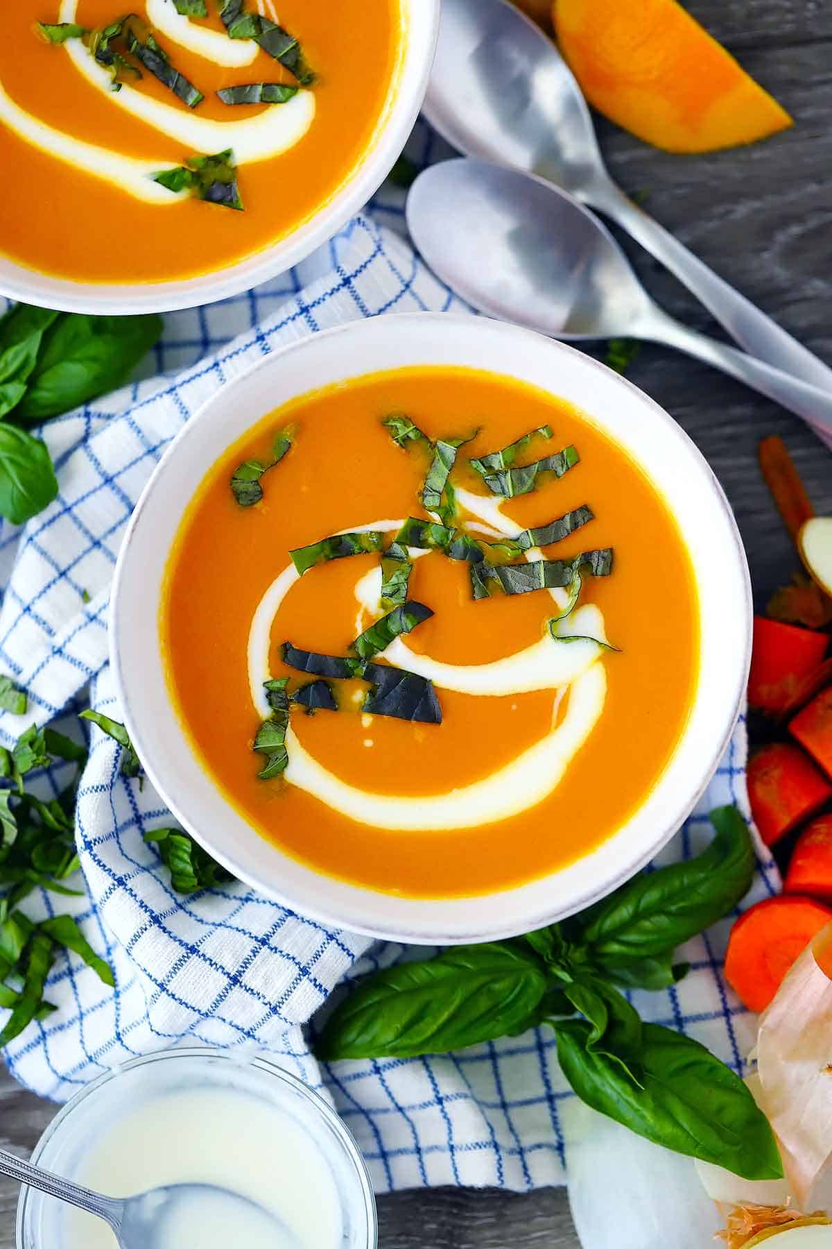 An overhead photo of a bowl of carrot ginger soup garnished with fresh basil.