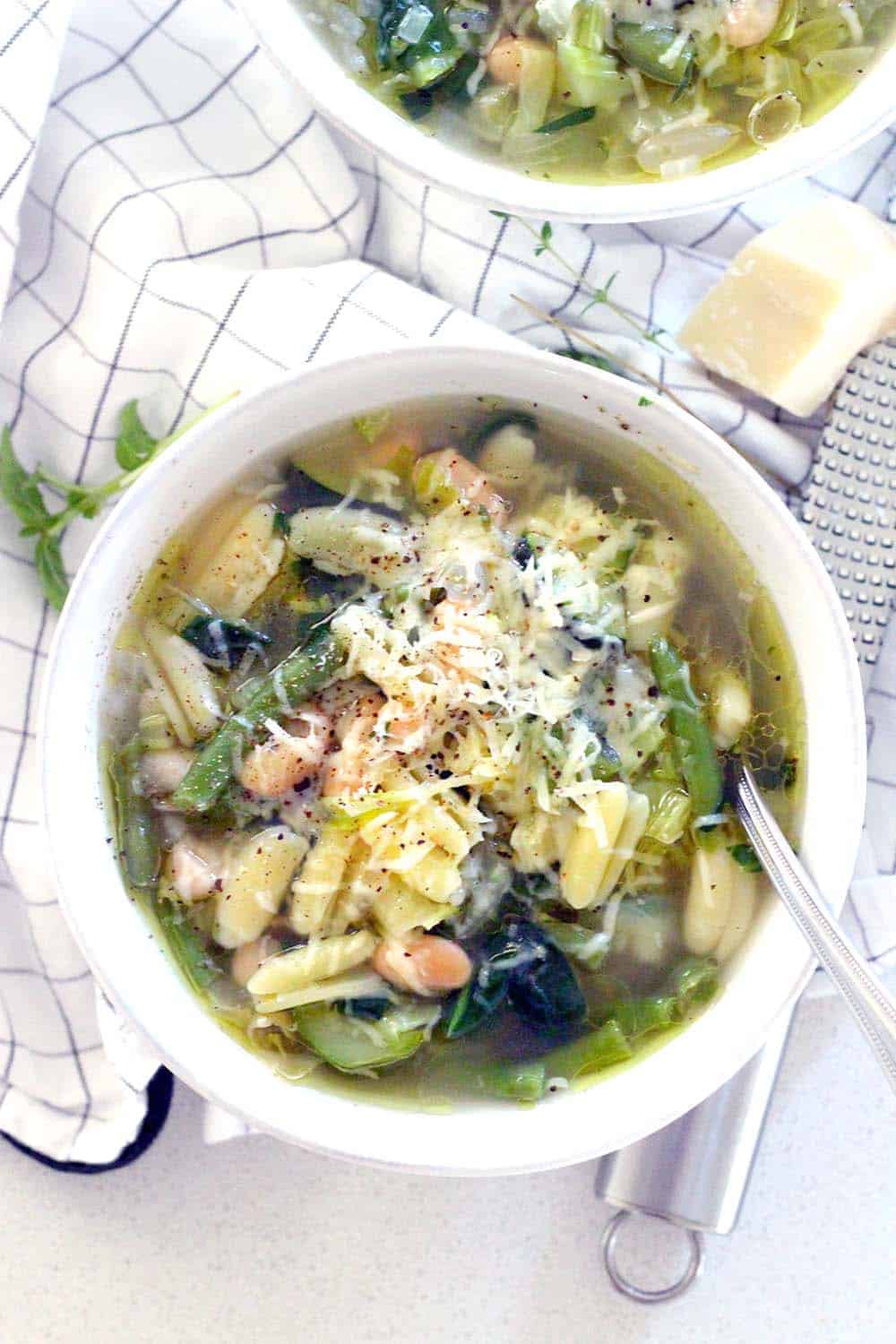 This minestrone soup is PACKED with healthy green veggies, fresh herbs, and topped with a drizzle of olive oil, Parmesan, and pepper. It comes together in 30 minutes and is freezable.