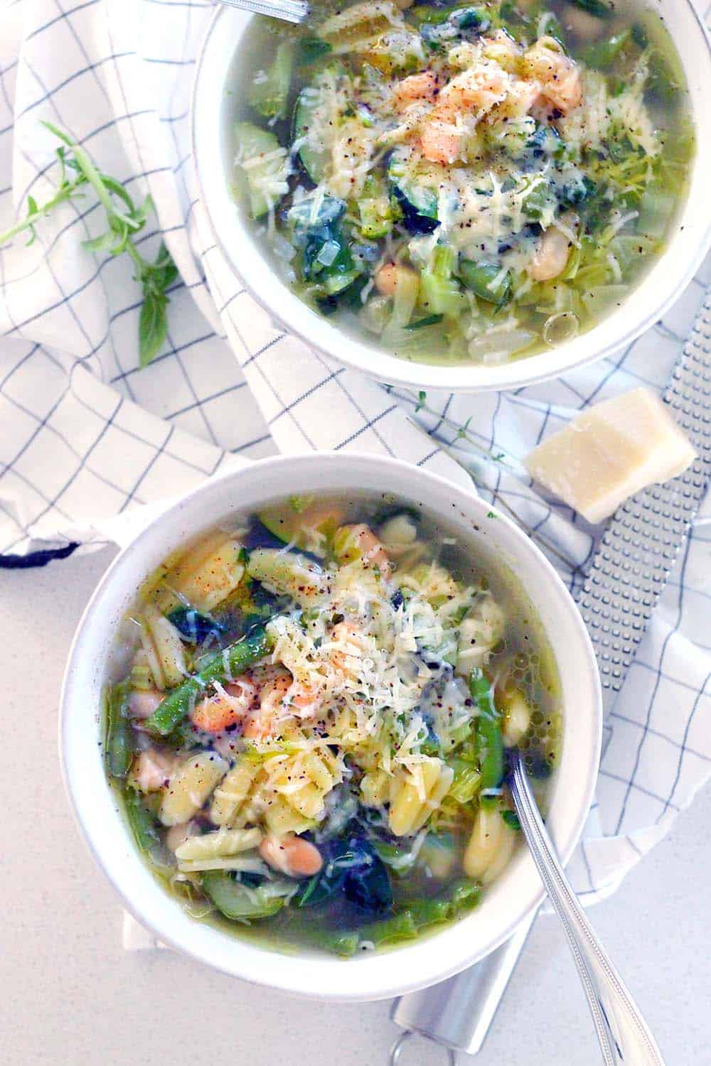 This minestrone soup is PACKED with healthy green veggies, fresh herbs, and topped with a drizzle of olive oil, Parmesan, and pepper. It comes together in 30 minutes and is freezable.