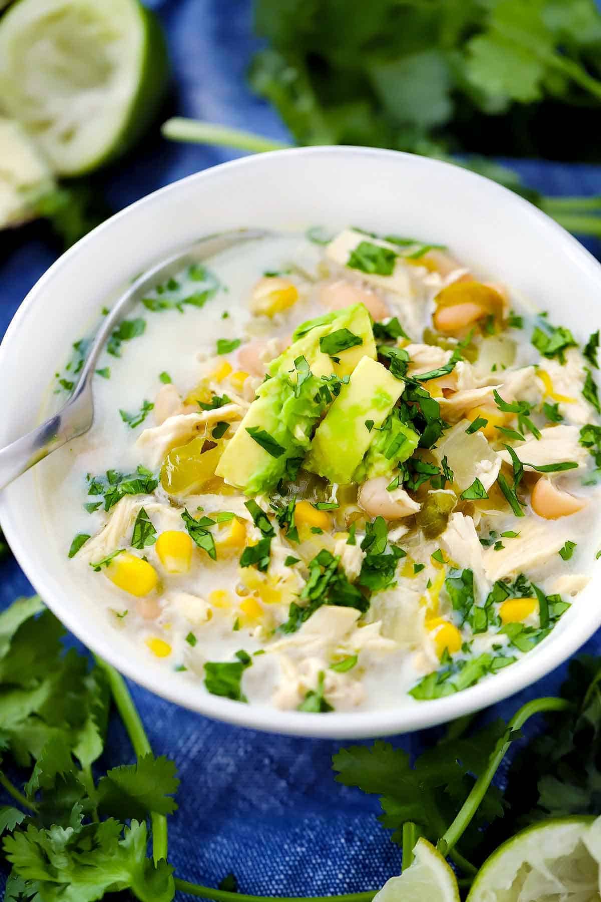 A white bowl filled with white chicken chili topped with avocado and cilantro.