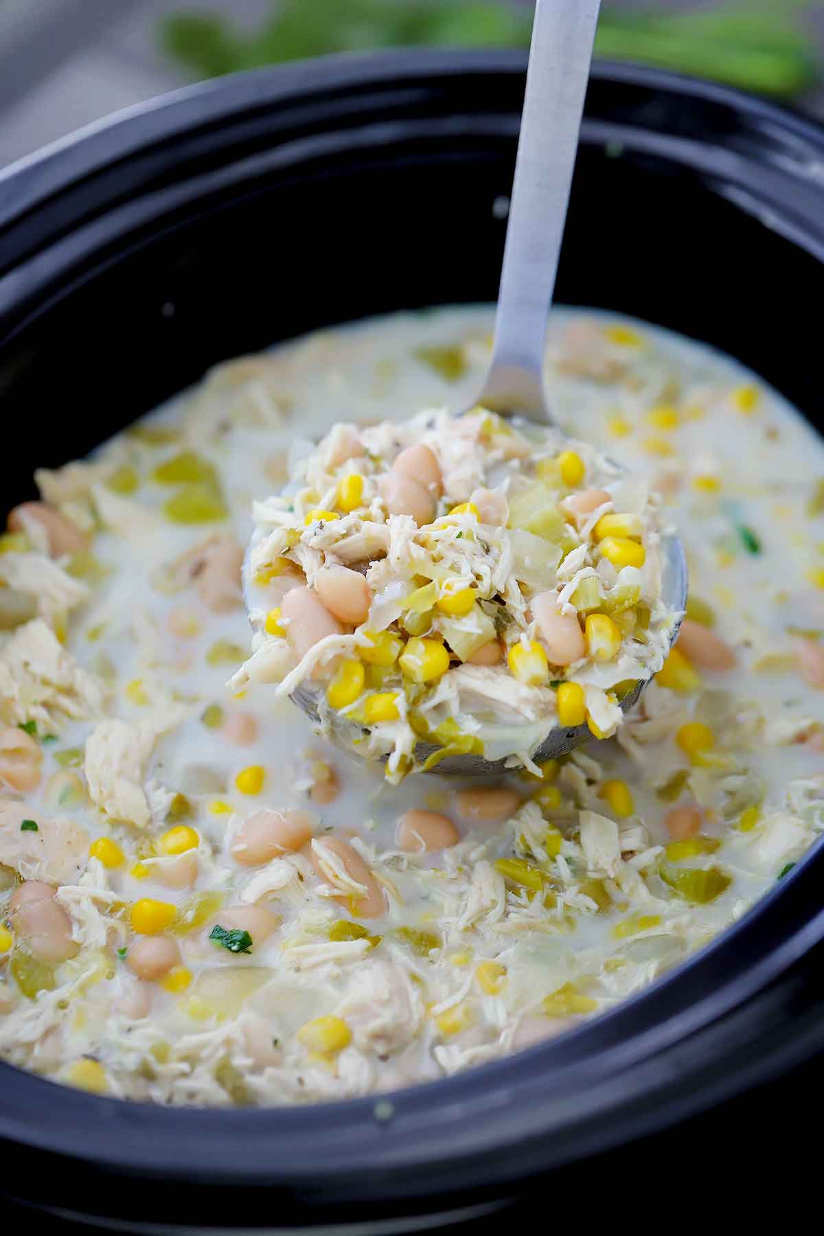 A ladle of white chicken chili in a slow cooker.
