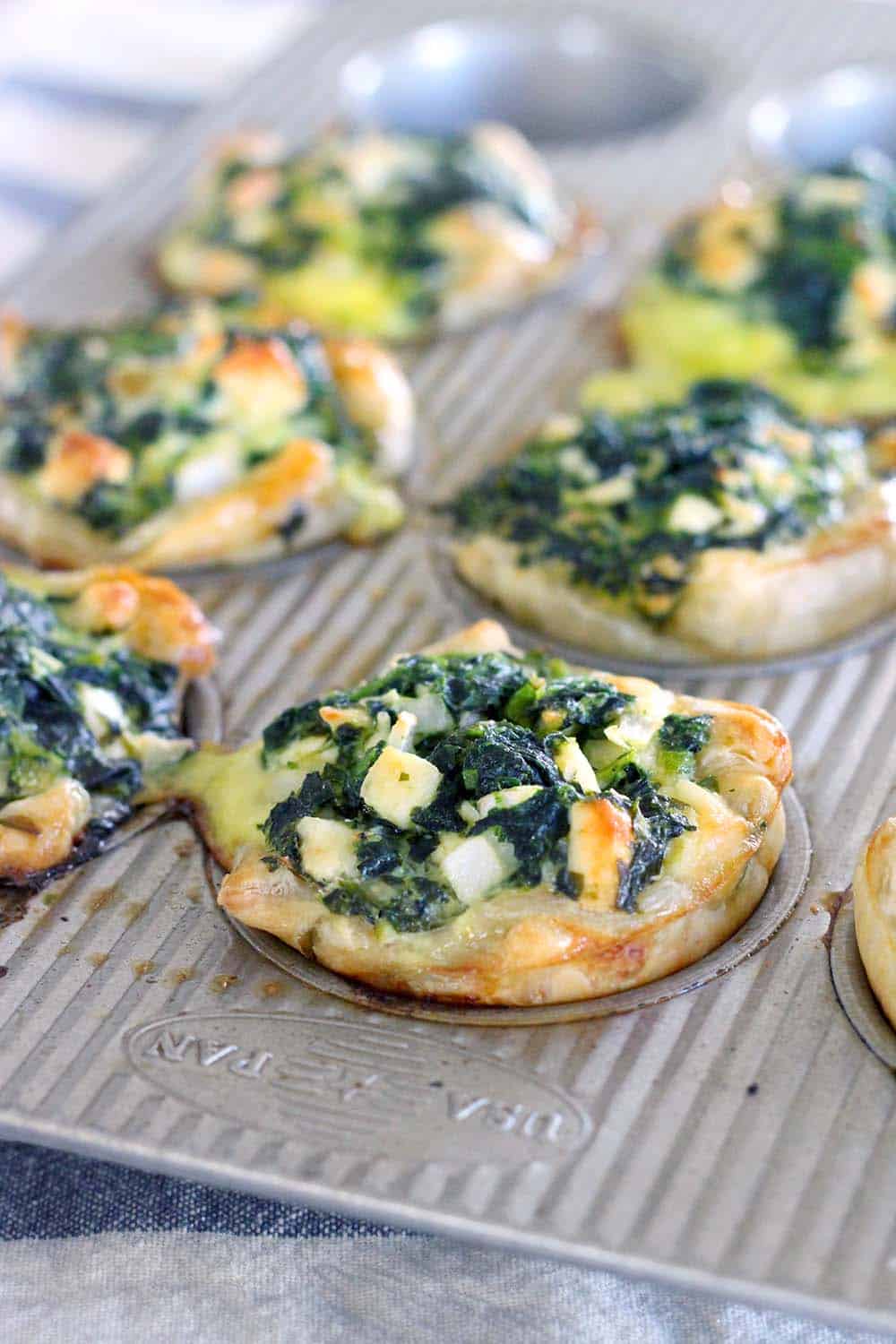 Mini spinach feta pies in a muffin pan.