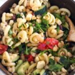 Square photo of close up overhead view of a Greek pasta salad with arugula, white beans, tomatoes, and herb vinaigrette.