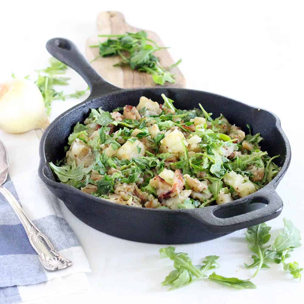This Skillet Potato Salad with Bacon and Arugula recipe is served warm with a sweet and tangy vinegar-based dressing. It's similar to German potato salad, Paleo and gluten-free, and the perfect side dish all year round!